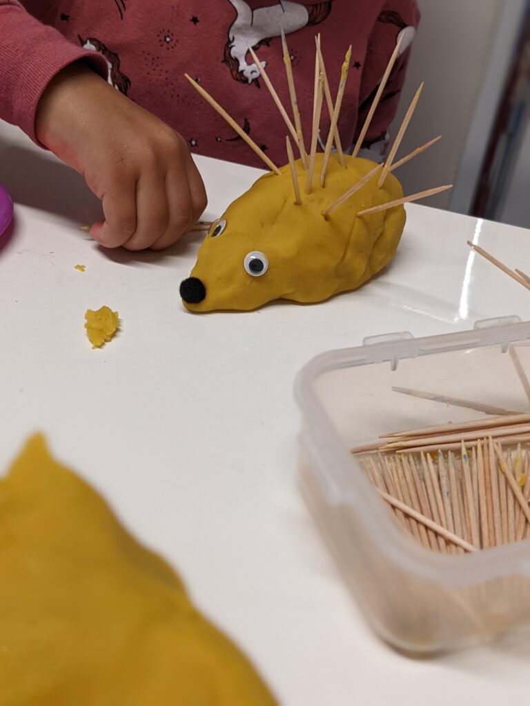 child putting tooth picks into playdough hedgehog