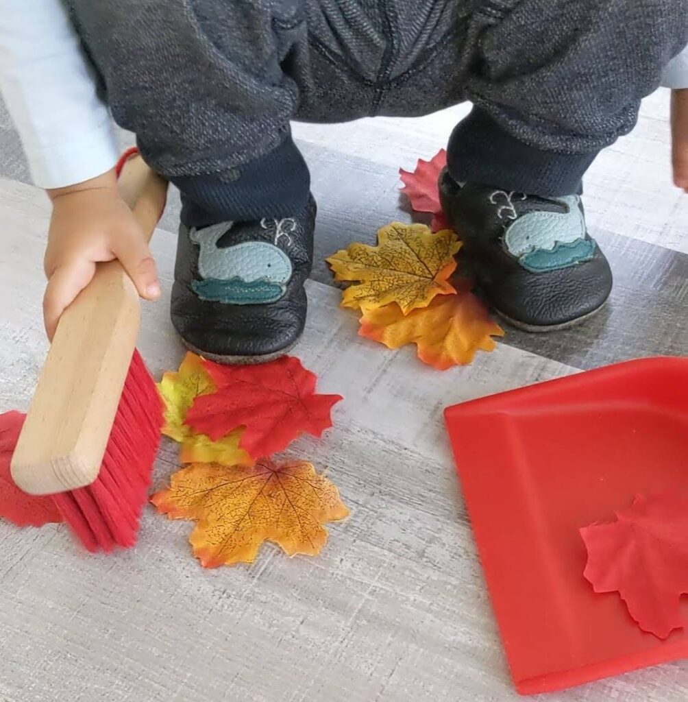 child sweeping fall leaves montessori
