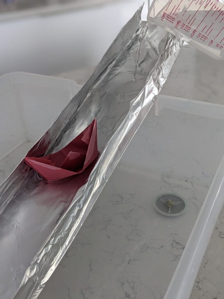 paper boat sliding down diy water spout as a Ramadan activity for kids