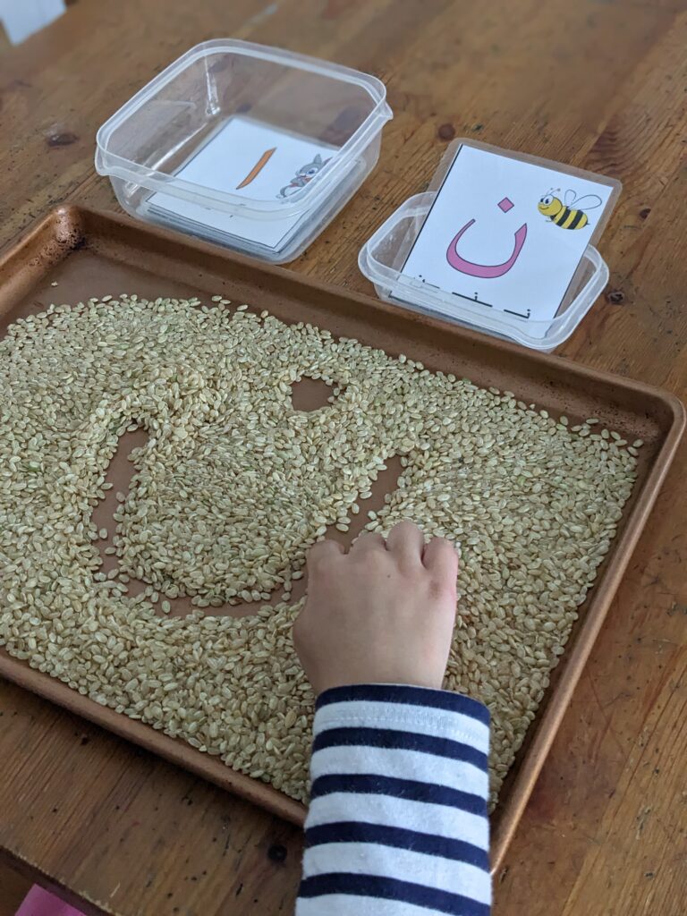 child writing in rice arabic letters as a Ramadan activity for kids